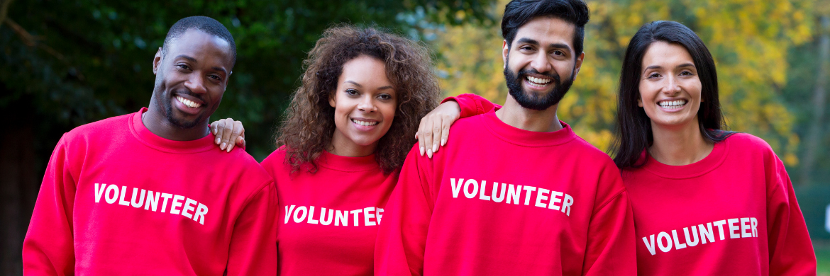 Group of four volunteers, two men and two women, smiling and wearing shirts with the word "Volunteer" on the front