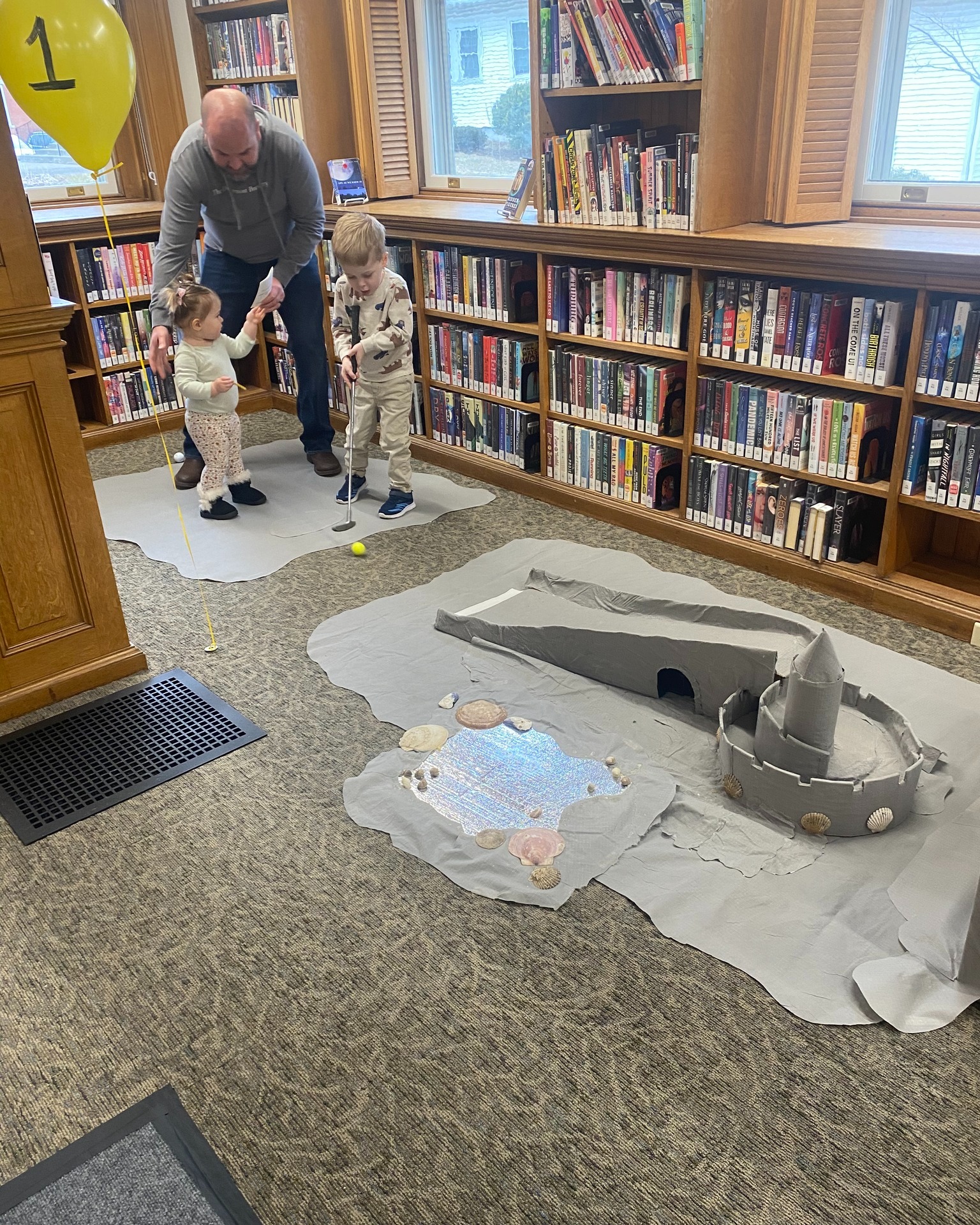 Castle mini-golf hole. 2 kids being helped by grandfather