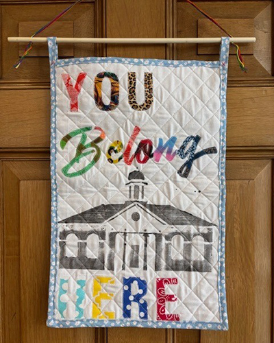 Knitted small blanket reading "Your Belong Here" with a church in the building