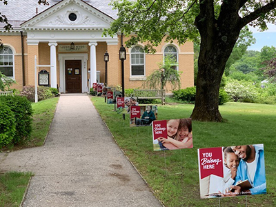 Yard signs lined up leading up to a large tan and white house