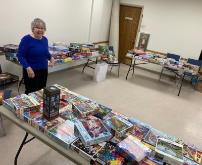 woman standing in front tables stacked with puzzles. 