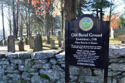 A historic cemetery with weathered gravestones and autumn trees. A sign reads "Old Burial Ground, Established c. 1740," conveying a respectful tone.