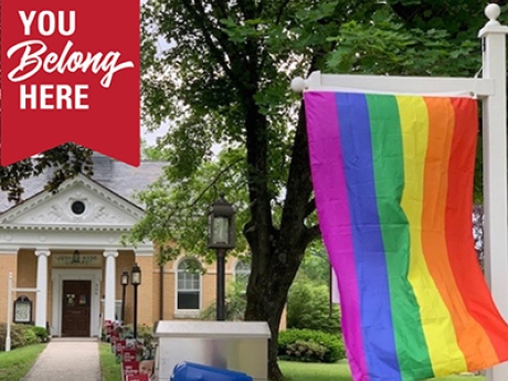 Pride flag hanging from a white post with a large house in the background