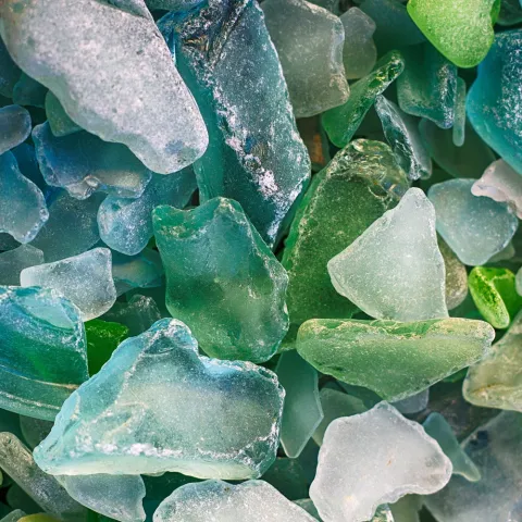 Colorful sea glass pieces in shades of blue and green, with smooth, frosted surfaces. They evoke a serene, beachcombed feeling.