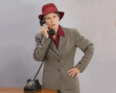 Woman in a red hat and beige suit holding a phone receiver