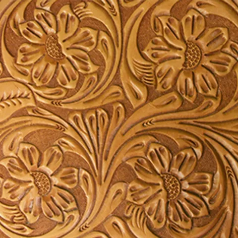 Ornate floral design tooled into a piece of brown leather, featuring large, detailed flowers with swirling leaves and stems, creating a vintage, textured look.