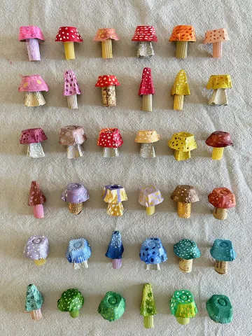 A pale background with a number of egg-carton mushrooms arranged in the color order of a rainbow.