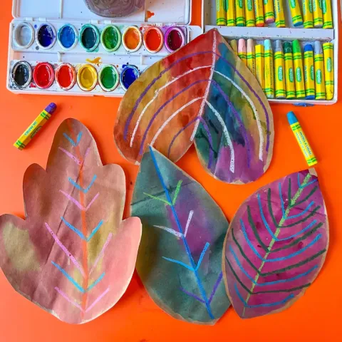 Handmade brown paper bag leaves painted with watercolors and drawn on with oil pastels.