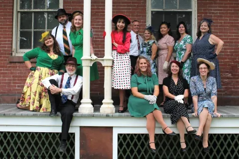 Group of people dressed in 1940's era clothing posing on a front porch