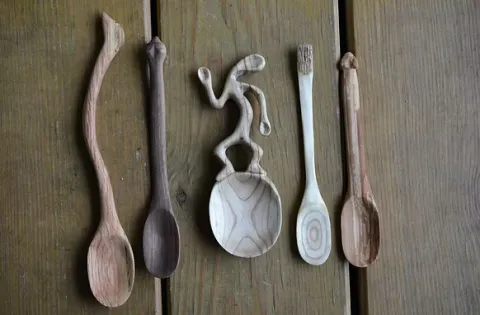 Five uniquely carved wooden spoons displayed on a wooden surface. Each spoon has a different shape and texture, showcasing creativity and craftsmanship.