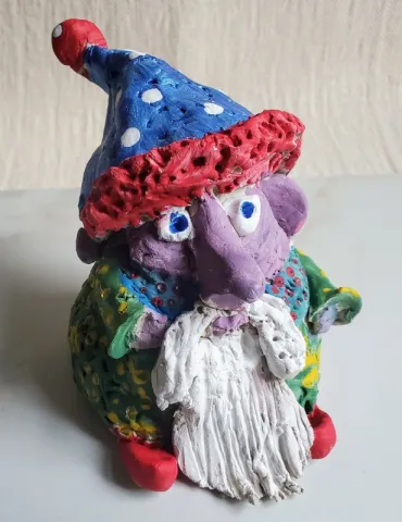 A handmade clay gnome with a white beard and colorful painted hat and shirt.