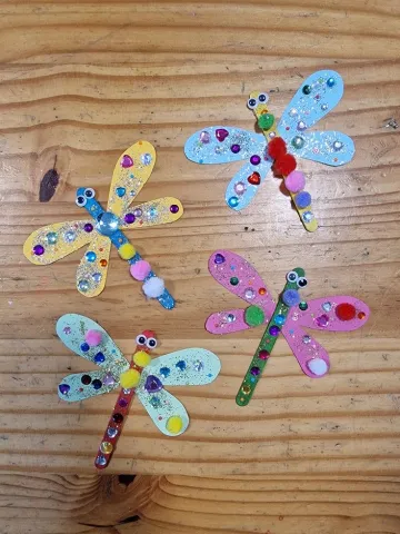 Popsicle stick dragonflies decorated with glitter, pompoms, and jewels.