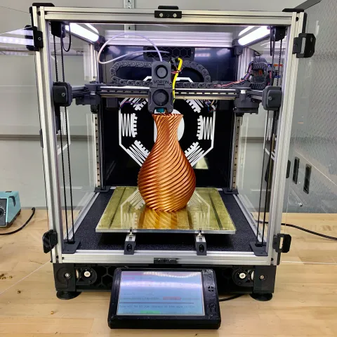 A 3D printer creating a small gold vase.