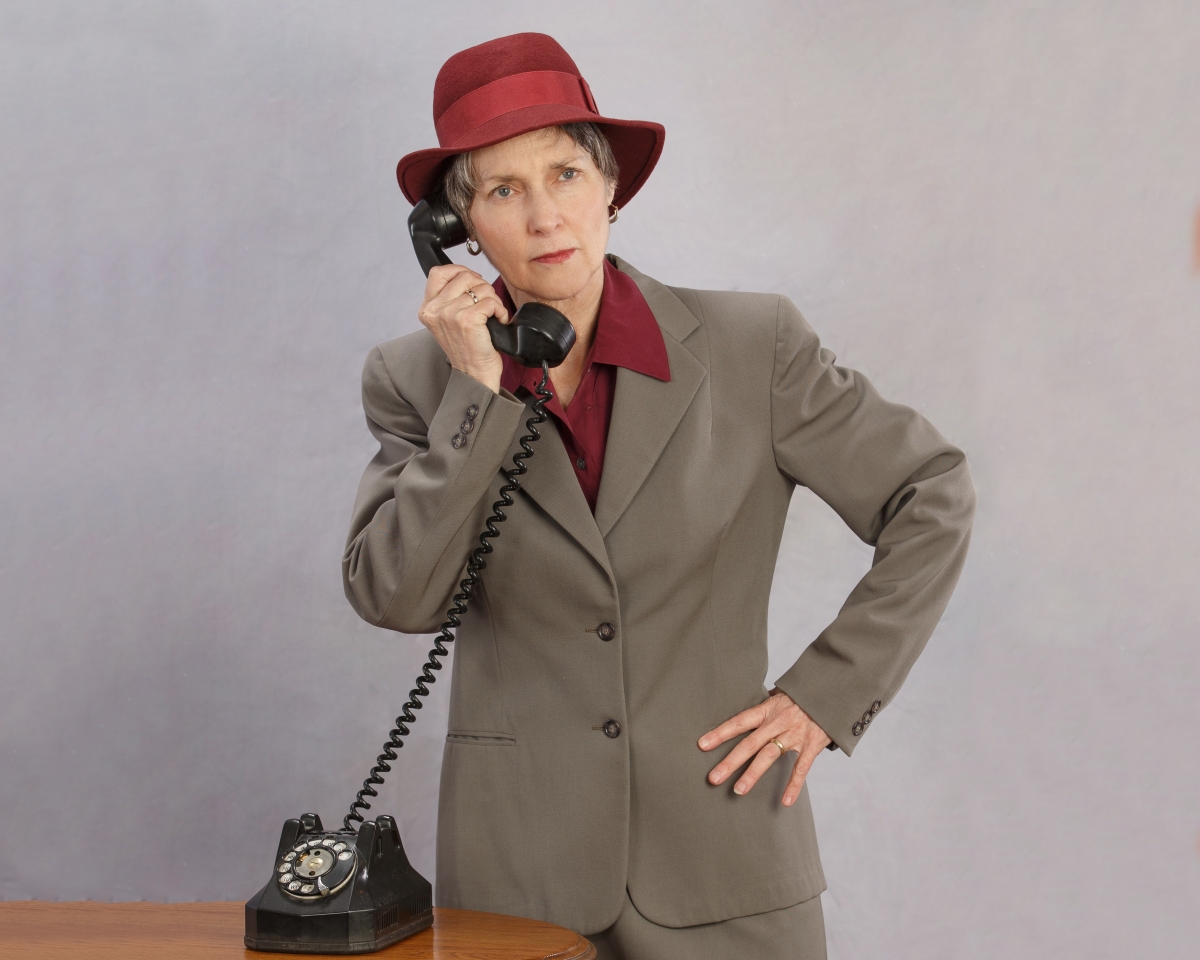 Woman in a red hat and beige suit holding a phone receiver