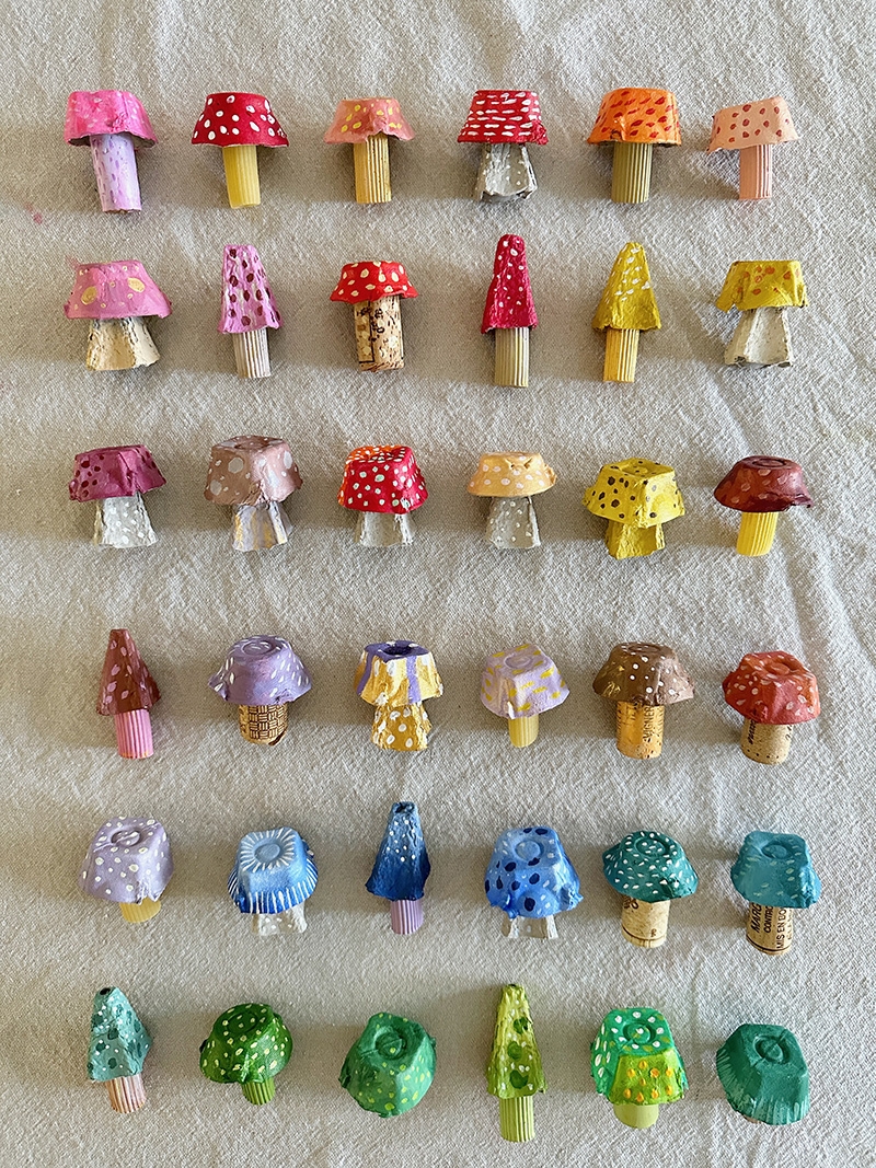 A pale background with a number of egg-carton mushrooms arranged in the color order of a rainbow.